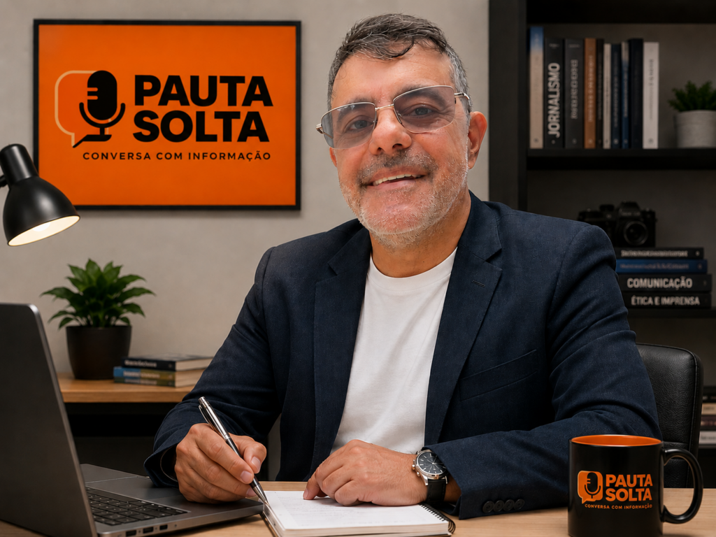 Retrato profissional do jornalista Adelar Dias Junior em ambiente corporativo, sentado à mesa de trabalho com notebook e bloco de anotações. Ao fundo, a identidade visual da Revista Pauta Solta em destaque, reforçando a atuação em comunicação e jornalismo. O ambiente é moderno, organizado e transmite credibilidade, proximidade e profissionalismo.